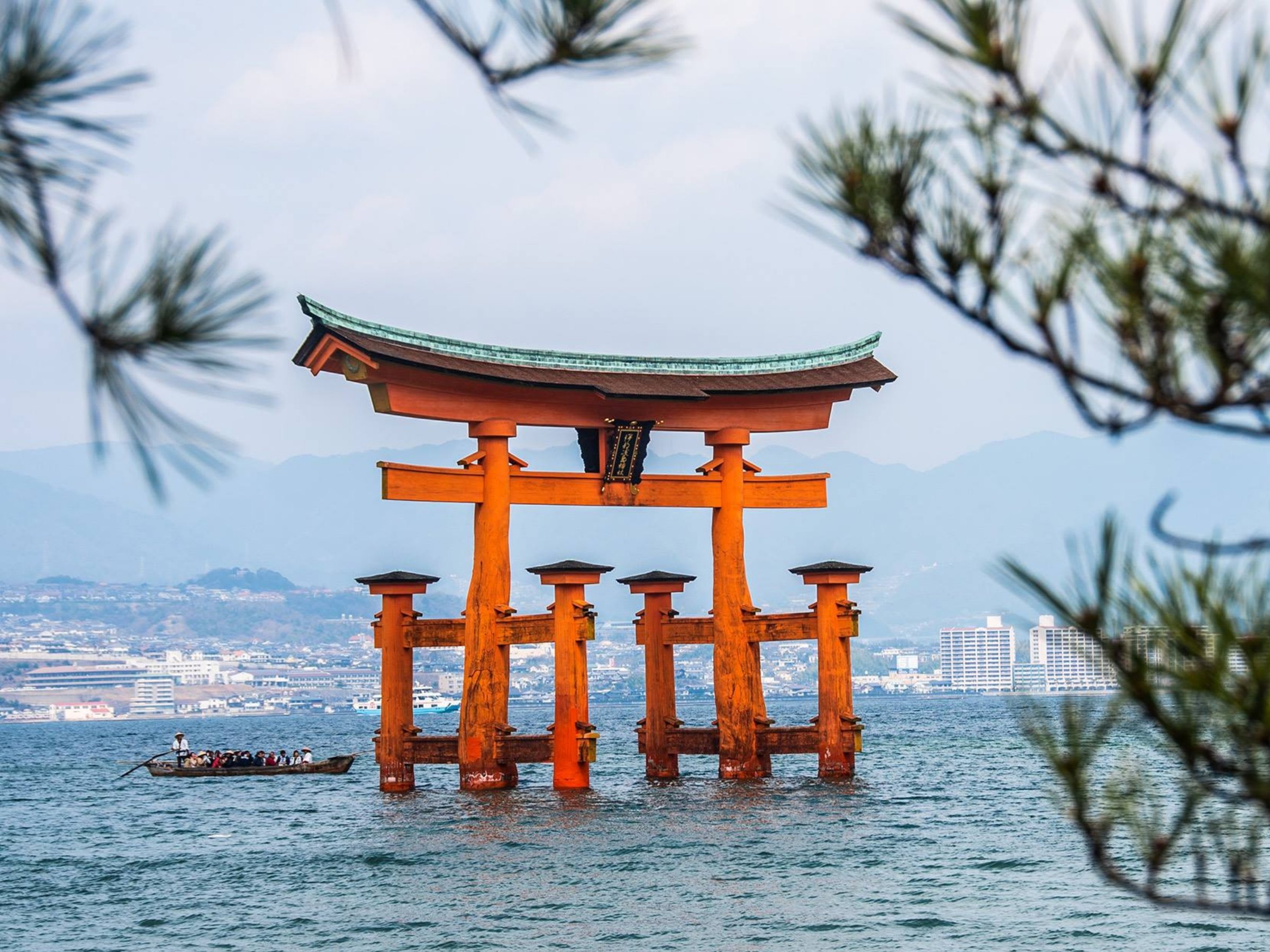Orange torii gate standing in the sea with a small boat nearby