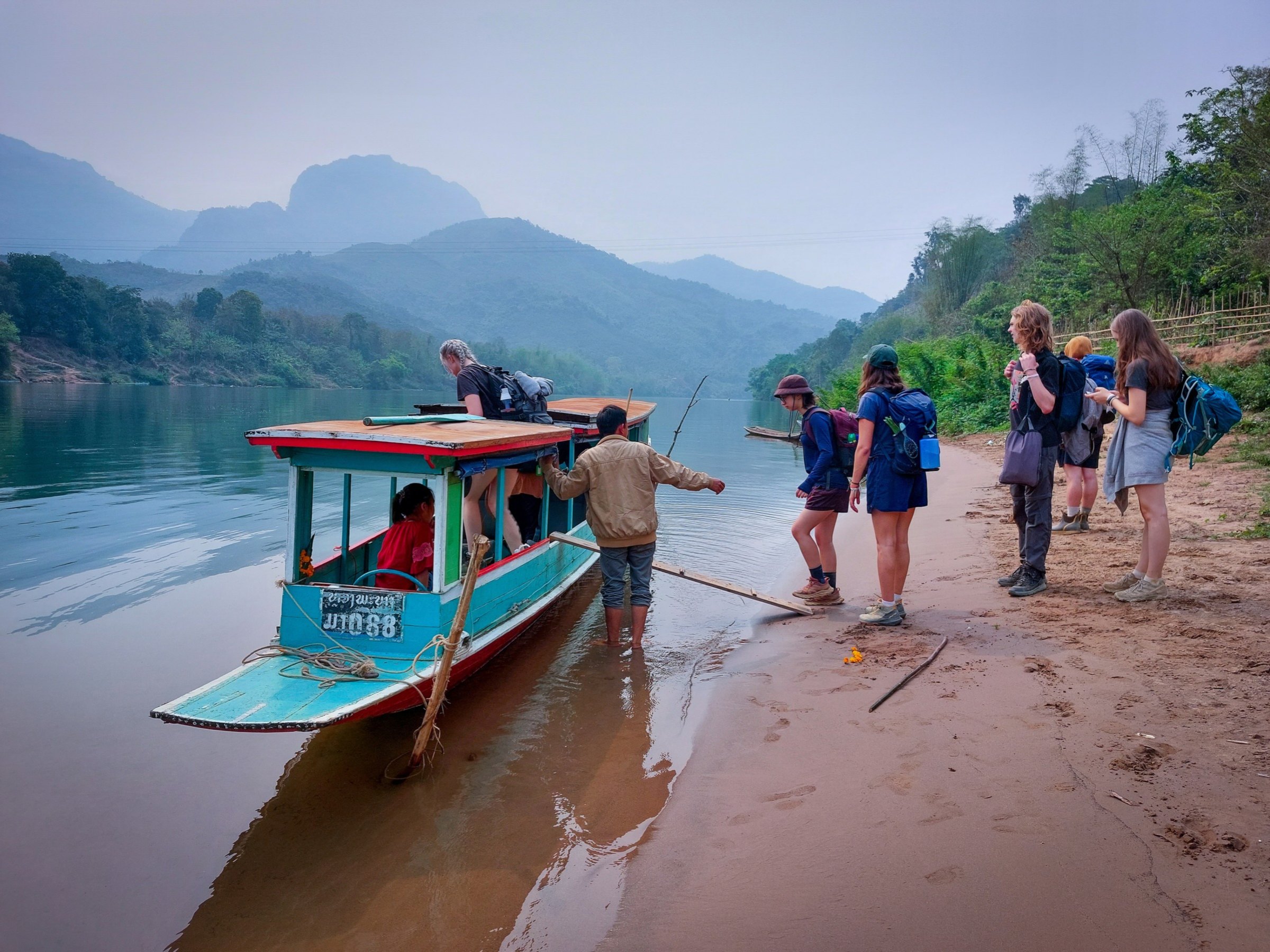 Group beside a river boat on a sandy riverbank