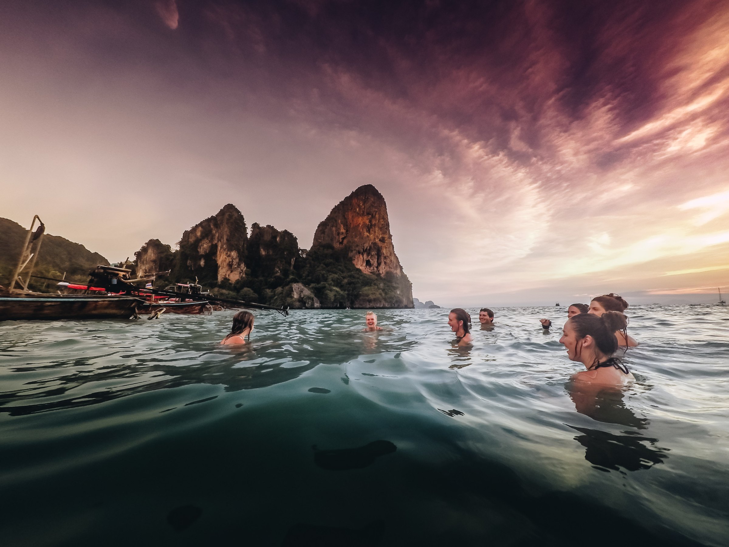 Snorkelers in turquoise water beside a boat flying the Thai flag