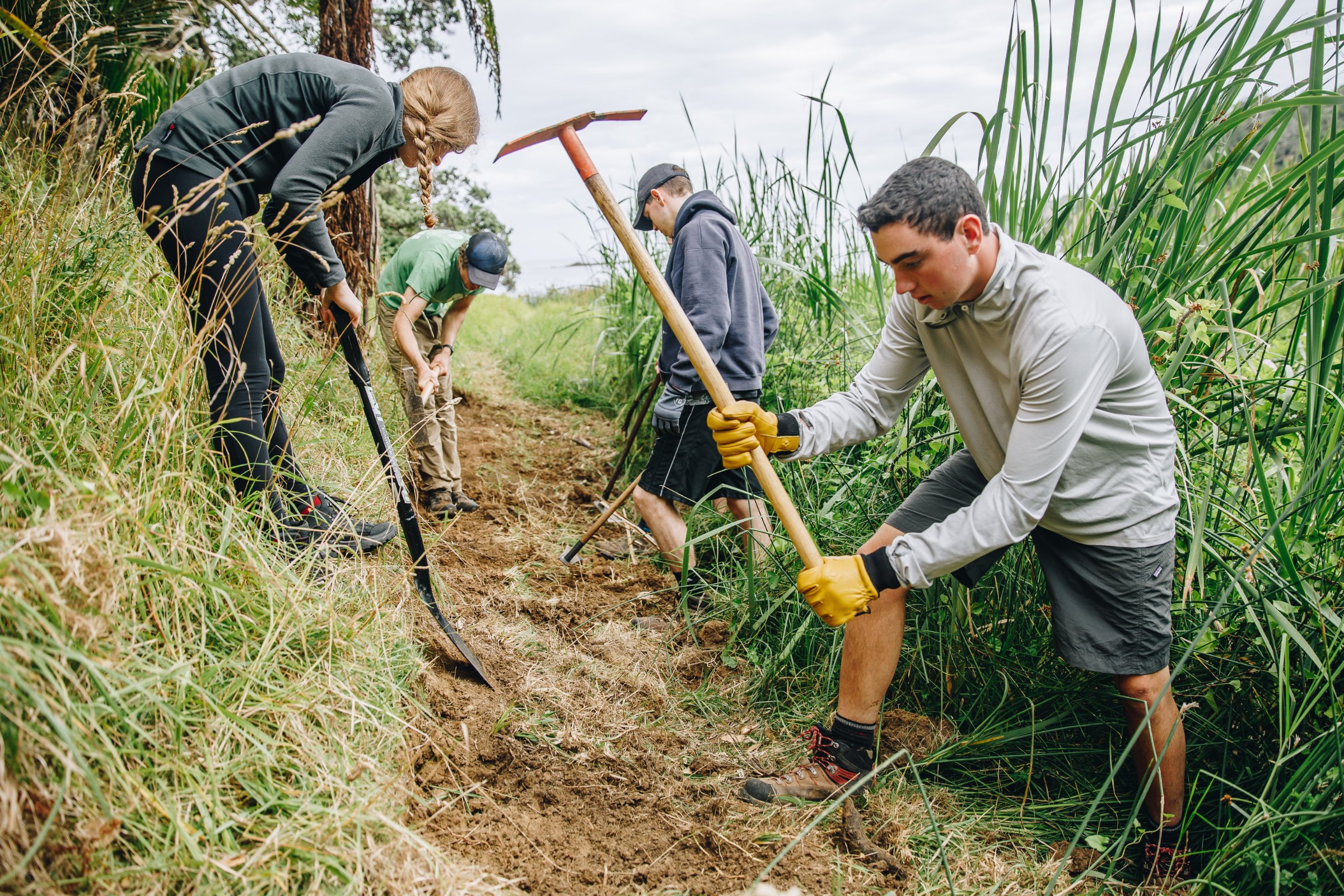 Smiling student in gloves kneeling to plant in a garden bed