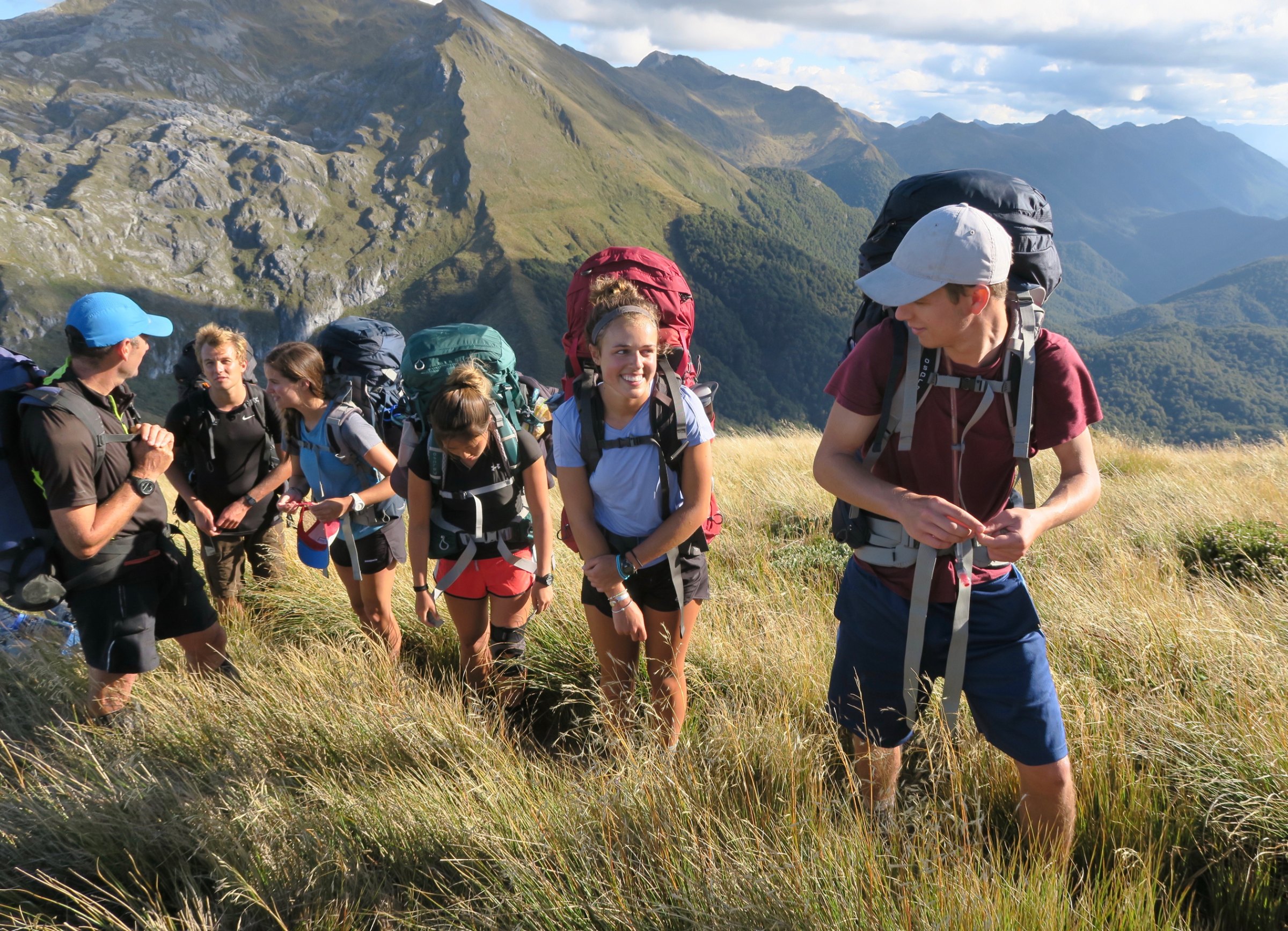 Group of hikers with backpacks walking toward snow-capped mountains