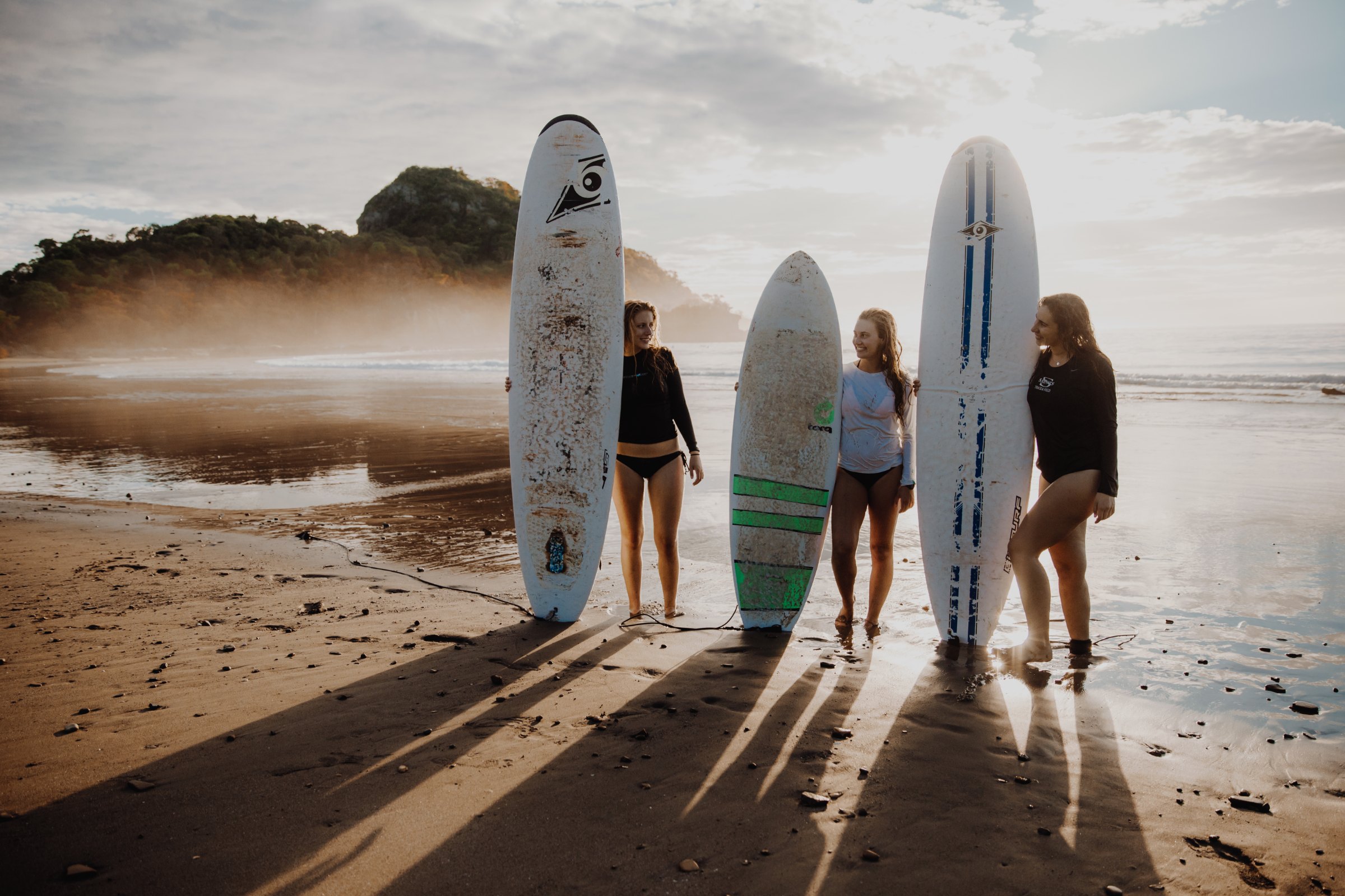Students lined up on a beach beside surfboards for a lesson
