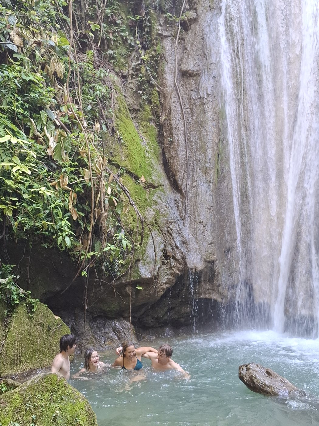 Students swimming beneath a jungle waterfall